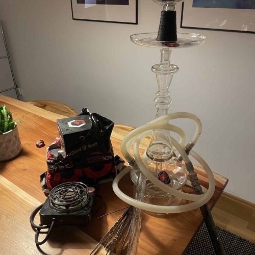 Rauch-Hookah mit Glasaufsatz, Schlauch und Zubehör auf Holztisch.