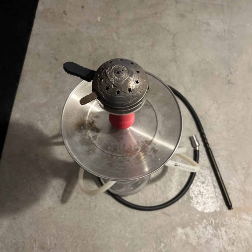Shisha mit Heizsystem, Glasbowl und Schlauch auf Betonboden.