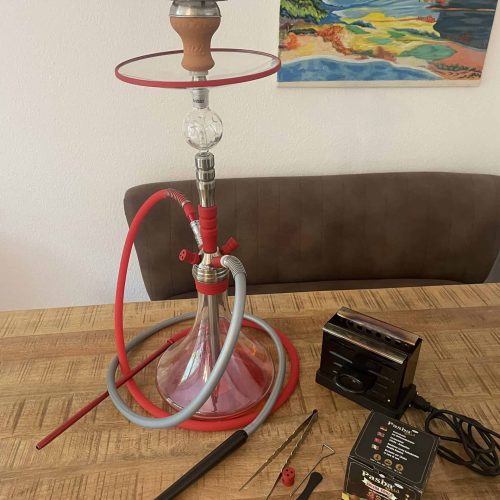 Rauchsäule mit Shisha, Schlauch, Kohlezange und Zubehör auf Holztisch.