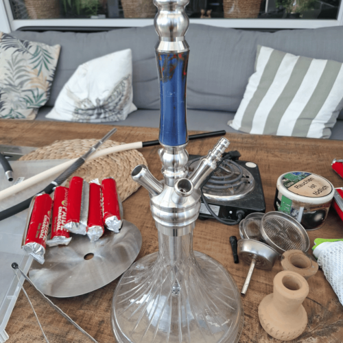 Shisha-Kopf mit blauer Glasbowl und Zubehör auf Tisch.