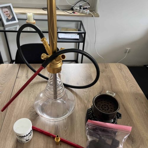 Shisha mit Glasbowl, Schlauch und Zubehör auf Holztisch.