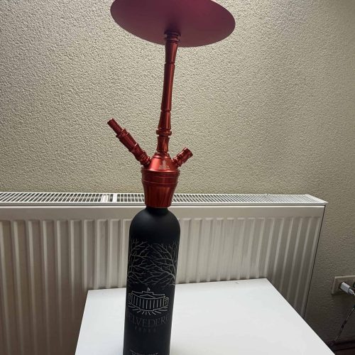 Dekorative Shisha mit rotem Kopf und Deckel, auf einem weißen Tisch neben Heizkörper.