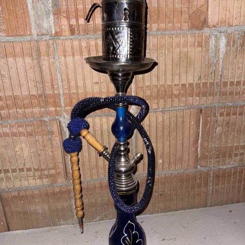 Gebrauchte Shisha mit Schlauch und Kopf, auf Boden gegen Ziegelwand.