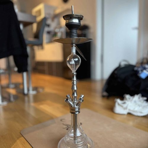 Wasserpfeife mit Glas- und Metallteilen, auf Holztisch stehend.