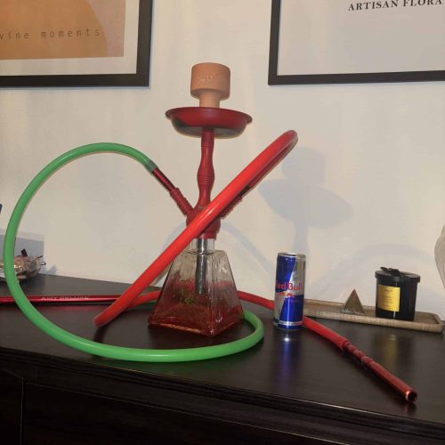 Bunte Wasserpfeife mit rotem Schlauch und Keramik-Kopf, auf einem schwarzen Tisch.