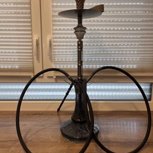 Alte Shisha mit zwei Schläuchen, auf Holztisch vor Fenster.