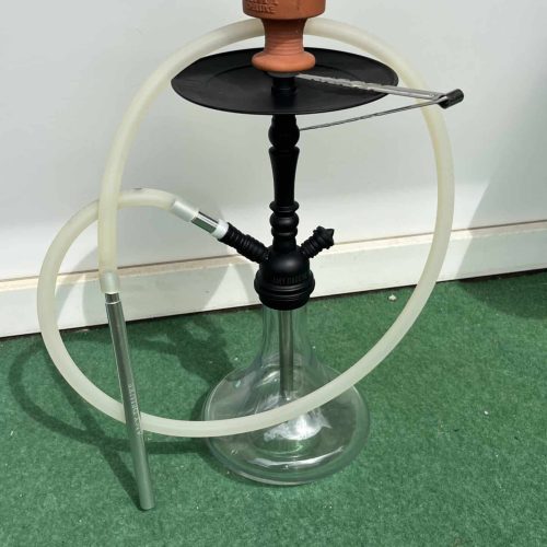 Shisha mit Glasbowl, Schlauch und Kohlezange auf grünem Teppich.