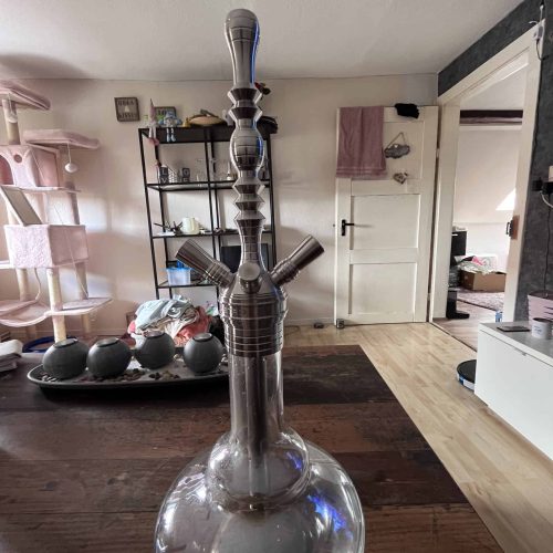 Große Glas-Shisha mit mehreren Schläuchen auf Holztisch im Wohnzimmer.