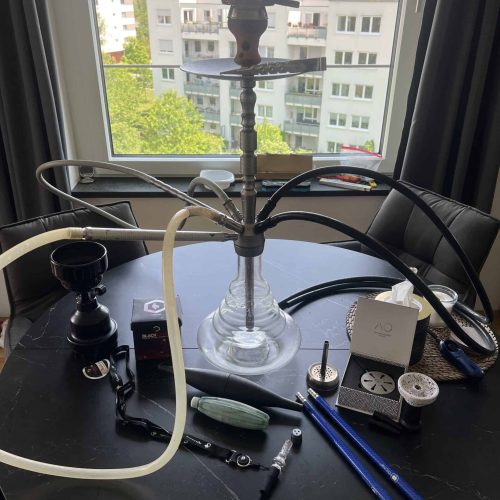 Rauchsäule und Shisha-Zubehör auf Fensterbank, Blick auf Stadt im Hintergrund.