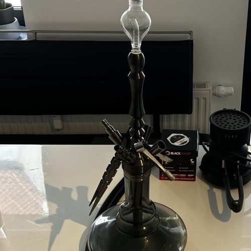 Shisha mit Glasaufsatz und Zubehör auf Tisch.