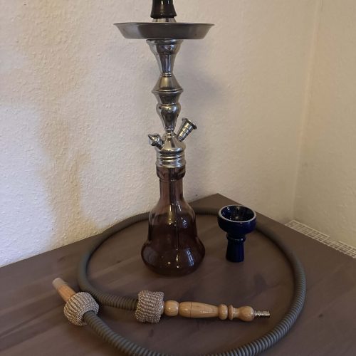 Shisha mit Glasbowl, Schlauch und Zubehör auf Tisch.