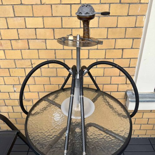 Rauchsäule mit Shisha, inklusive Schlauch und Tabak, auf Balkon vor Ziegelwand.