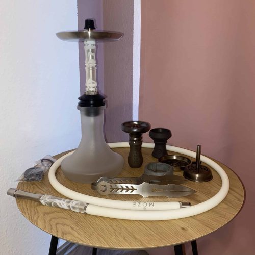 Shisha mit Zubehör auf einem runden Holztisch, inklusive Schläuchen und Kerzenhalter.