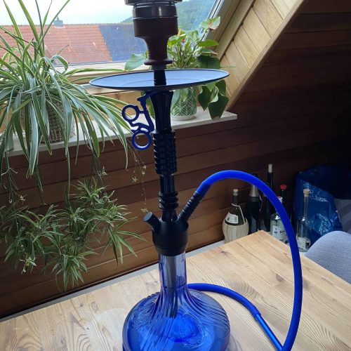 Blaue Wasserpfeife mit Glasbasis, Schlauch und Zubehör auf Holztisch im Raum.
