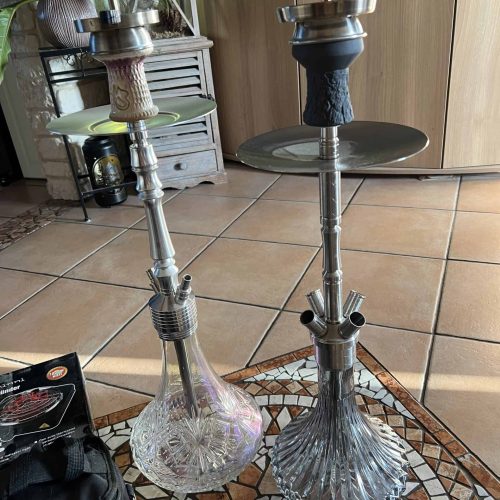 Zwei Shishas mit Glasbasis und Metallrohren, bereit für den Gebrauch.