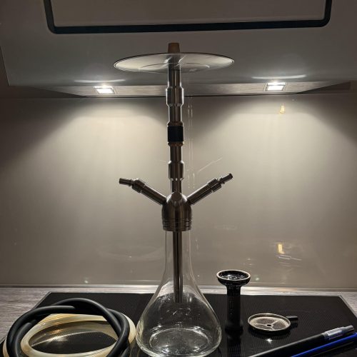 Glas-Shisha mit Schlauch, Zange und Tabakdose auf Herdplatte.