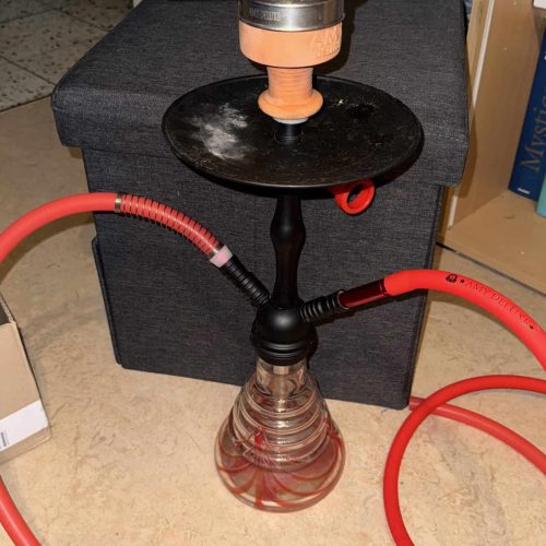 Shisha mit Wasserpfeife, Schlauch und Zubehör auf Tisch.