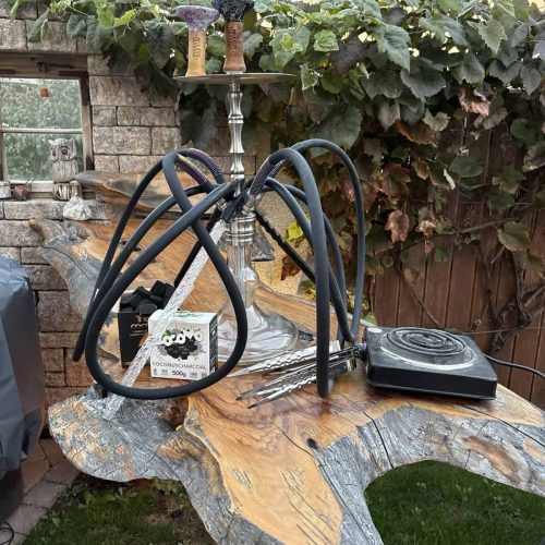 Rauch-Hookah mit Schlauch, Tabak und Zubehör auf Holzplatte im Garten.