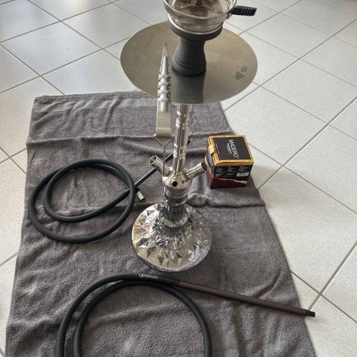 Shisha mit Glasbowl, Schlauch und Kohlebox auf Teppich.