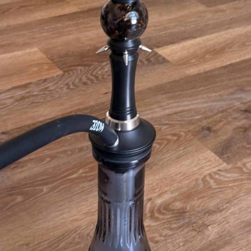 Shisha mit Glasbowl, Metallaufsatz und Holzsockel auf Holzboden.