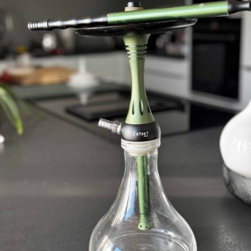Moderne Shisha mit Glasgefäß und Rauchsäule auf Tisch.