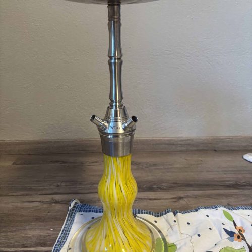 Rauch-Hookah mit gelbem Glas und Metallaufsatz, auf Tisch.