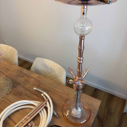 Shisha-Kopf mit Glasbowl, Schlauch und Zubehör auf Tisch.