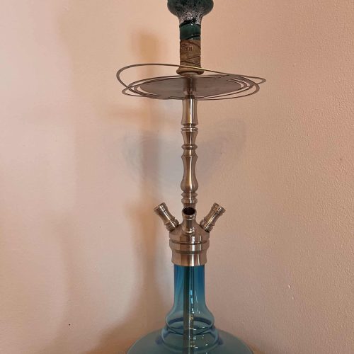 Hookah mit Glasbasis und Metallaufsatz, auf Tisch stehend.