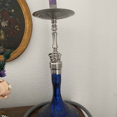 Alte Shisha mit blauer Glasbasis und Metallteilen, auf einem Tisch.