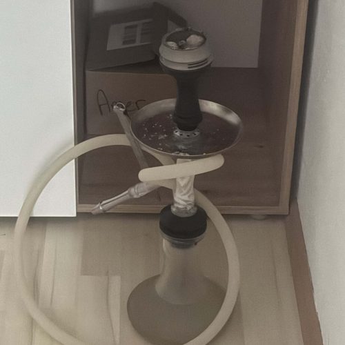 Shisha mit schwarzer Glasbowl und Schlauch, auf Boden stehend.