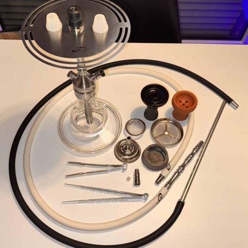 Shisha mit Glasbowl, Schlauch und Zubehör, auf weißem Tisch.