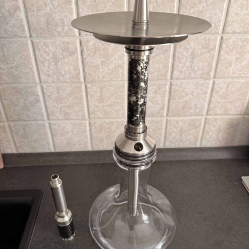 Shisha mit Glasbowl, Metallaufsatz und Zubehör auf Tisch.