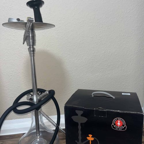 Shisha mit Glasbowl, Metallrohr und Zubehör im Raum.