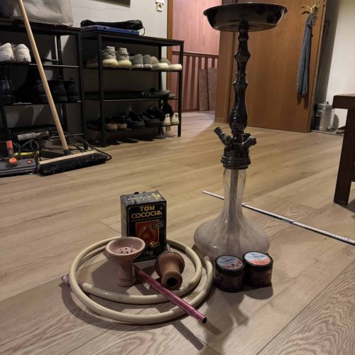 Shisha-Set mit Wasserpfeife, Tabak, Kohle und Zubehör auf Holzboden.