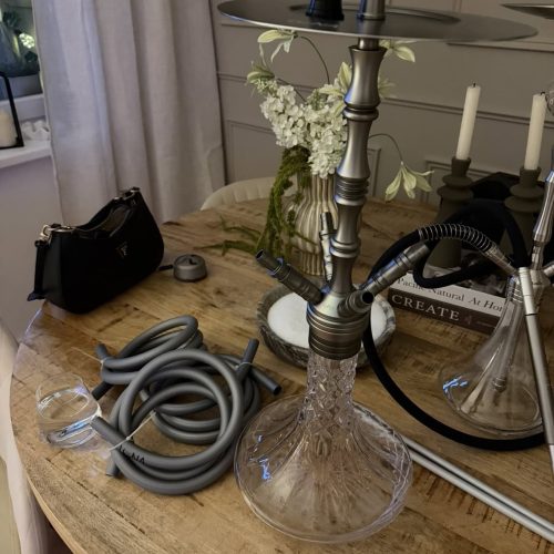 Shisha-Kohlenzange und Glasbowl auf Holztisch, Dekoration im Hintergrund.