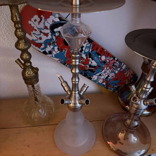 Shisha mit Skateboard im Hintergrund, auf Holzregal.