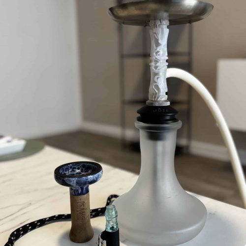 Rauchsäule mit Shisha, Kohlezange und Schlauch auf Tisch.