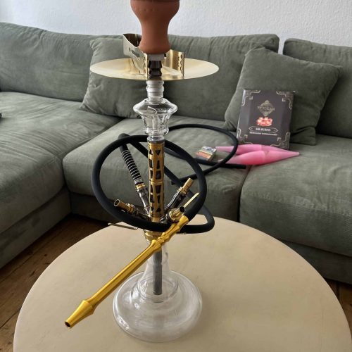 Shisha mit Glasbowl, Schlauch und Tabakpackung im Wohnzimmer.