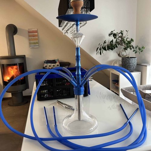 Rauchersäule mit blauer Silikonschlauch auf weißem Tisch, modernes Wohnzimmer mit Kamin und Pflanzen.