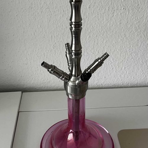 Shisha mit Glasbasis und Metallstücken, auf weißem Tisch.