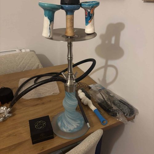 Rauch-Hookah mit buntem Kopf, Schlauch und Zubehör auf Tisch.
