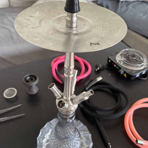 Shisha mit Glasbasis, Tabak und Zubehör auf Tisch.
