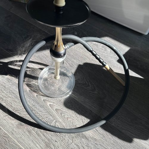 Schisha mit Glas, Schlauch und Kopf, auf dunklem Holzboden.