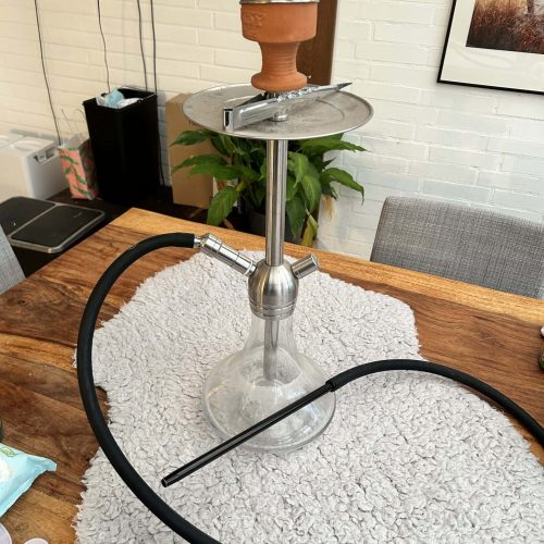 Shisha mit Glasgefäß, Kopf und Schlauch auf Tisch.