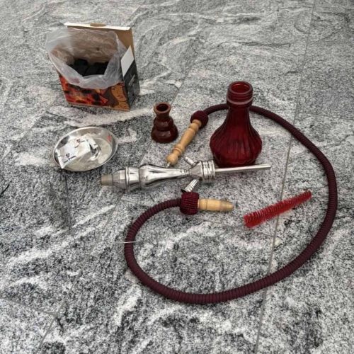 Shisha mit Glasbowl, Schlauch und Zubehör auf Steinboden.