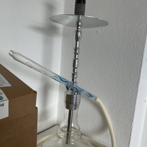 Shisha mit Glasbowl, Metallrohr und Düse, auf weißem Tisch.