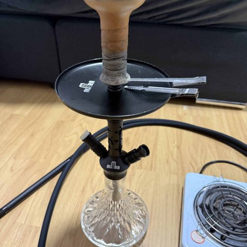 Shisha mit Glasbase, Kopf und Schlauch auf Holztisch.