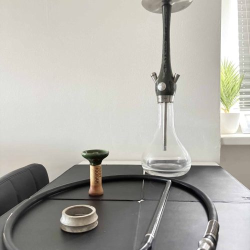 Shisha mit Glasbowl, Schlauch und Kopf auf Tisch.
