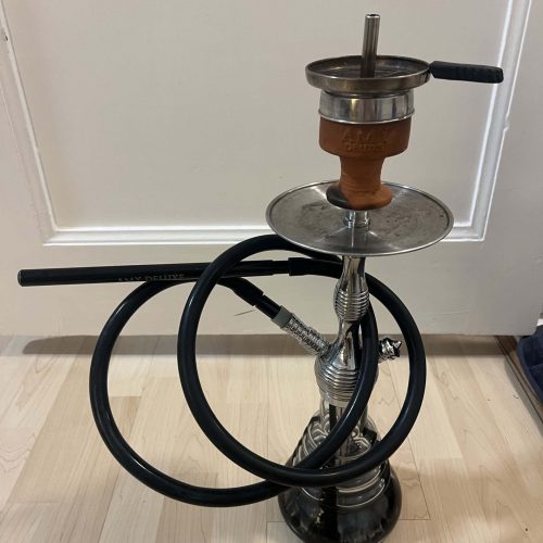 Shisha mit Rauchsäule und Schlauch, auf Holzboden vor weißer Tür.