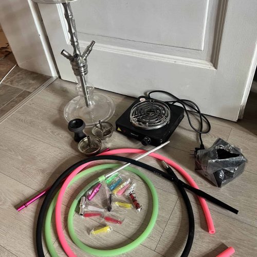 Shisha mit Glaskopf, Schläuchen und Heizgerät auf Boden.